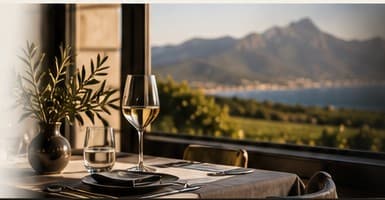 A terrace table with a glass of wine and an olive branch, mountains and vineyards beyond