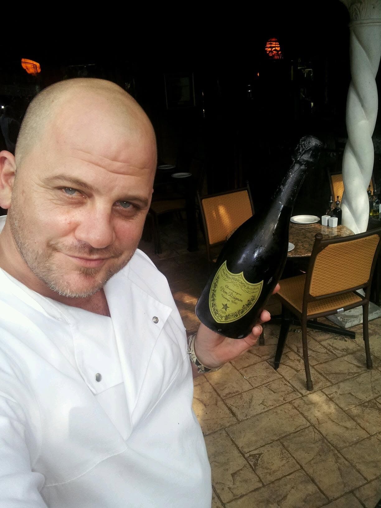 Paul in his chef jacket on the restaurant terrace, holding a bottle of Dom Pérignon