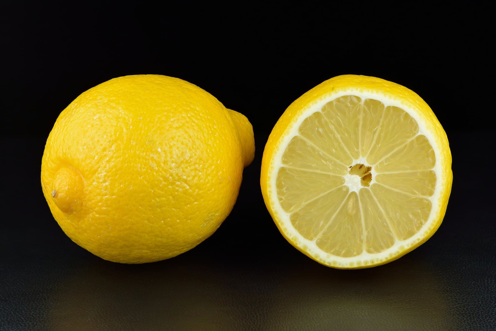 A whole lemon beside a halved lemon showing its segments, on a dark background