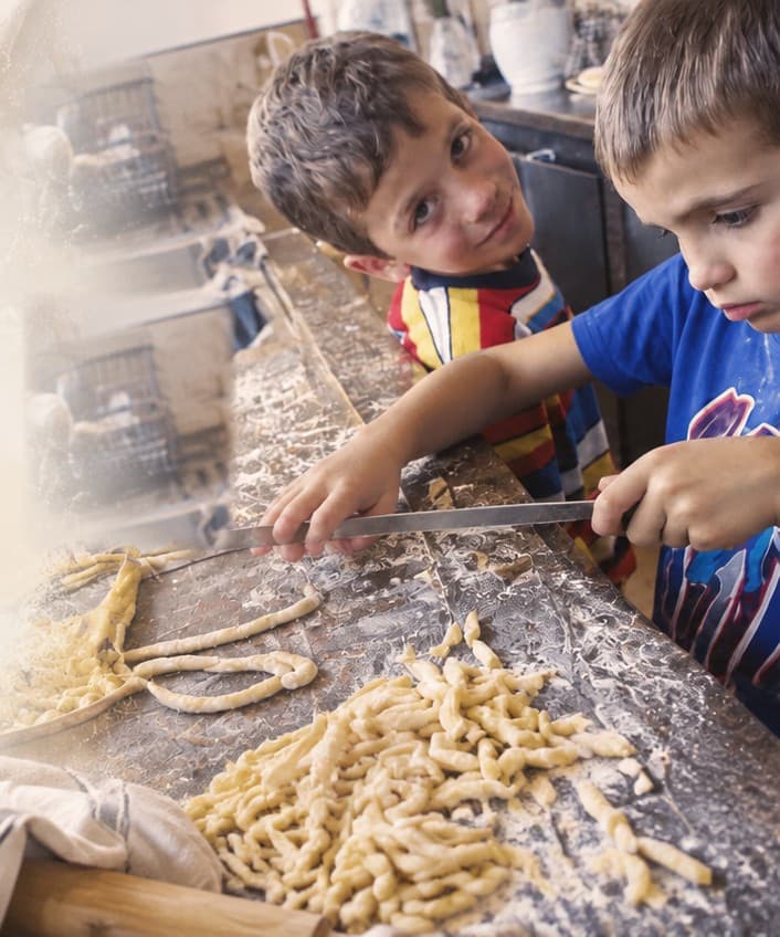 Two boys cutting fresh pasta on a floured wooden board