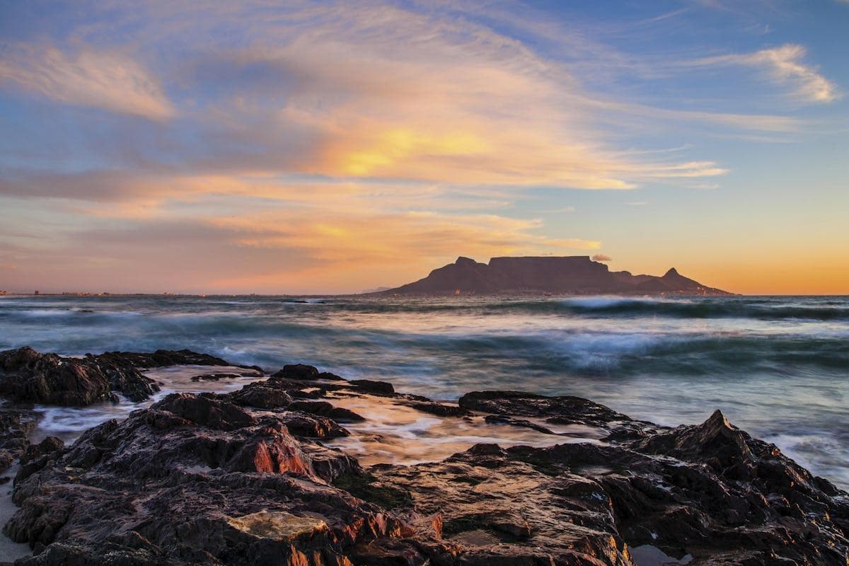 Table Mountain across the bay at dusk, waves breaking over dark rocks in the foreground