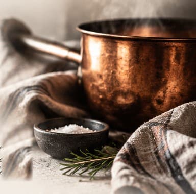 A steaming copper pot, a bowl of salt and a sprig of rosemary on linen