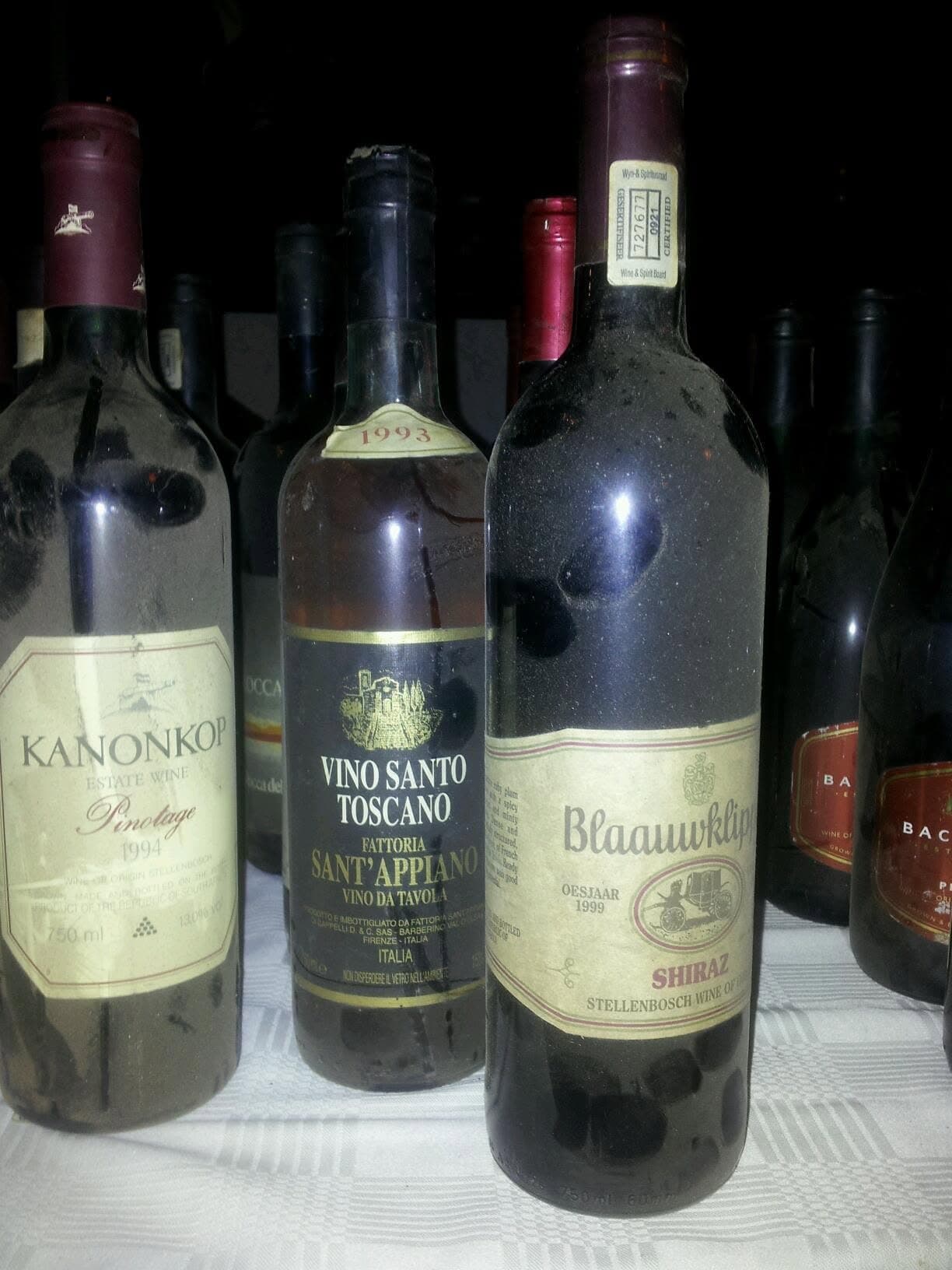 Old bottles of Kanonkop and Vin Santo among others, labels worn, lined up on a table
