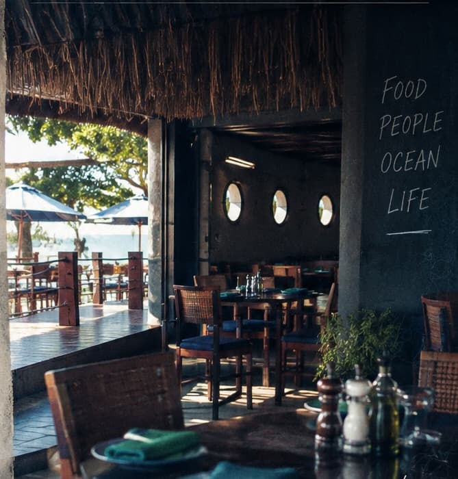 Inside 40 Knots: the thatched terrace, tables laid with blue and green napkins, portholes on the wall