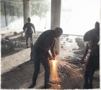 Two people welding on the floor, sparks flying