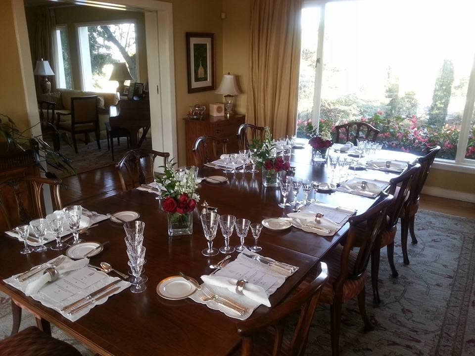 The dining room at the residence, the long table laid with crystal, silver and red roses, the garden through the windows