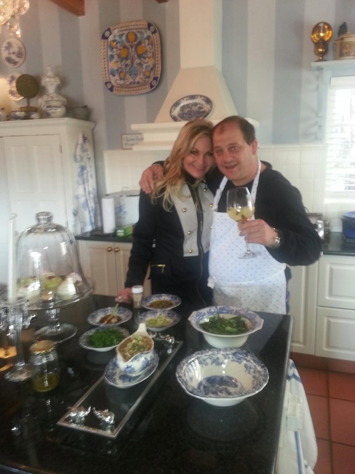 Paul in an apron beside a host in a private kitchen, the mise en place laid out on the island