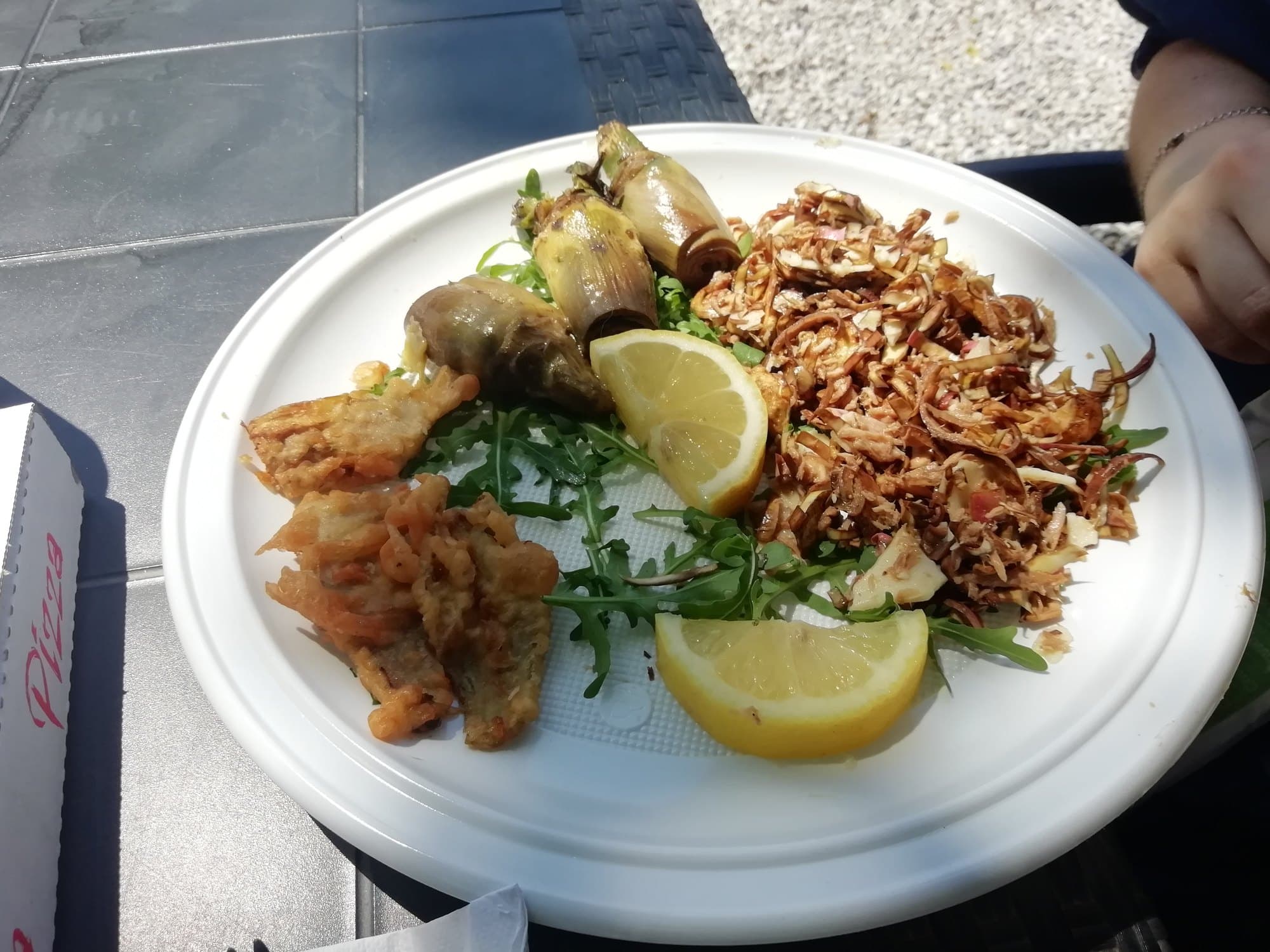 Cooked artichokes prepared three ways on a plate with lemon and rocket