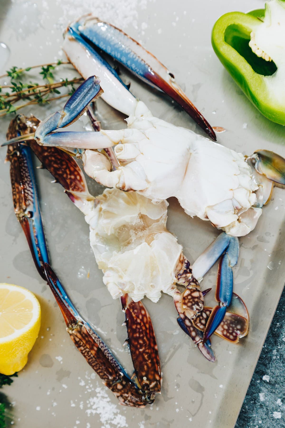 Blue crab claws and body on a steel tray with lemon and green pepper