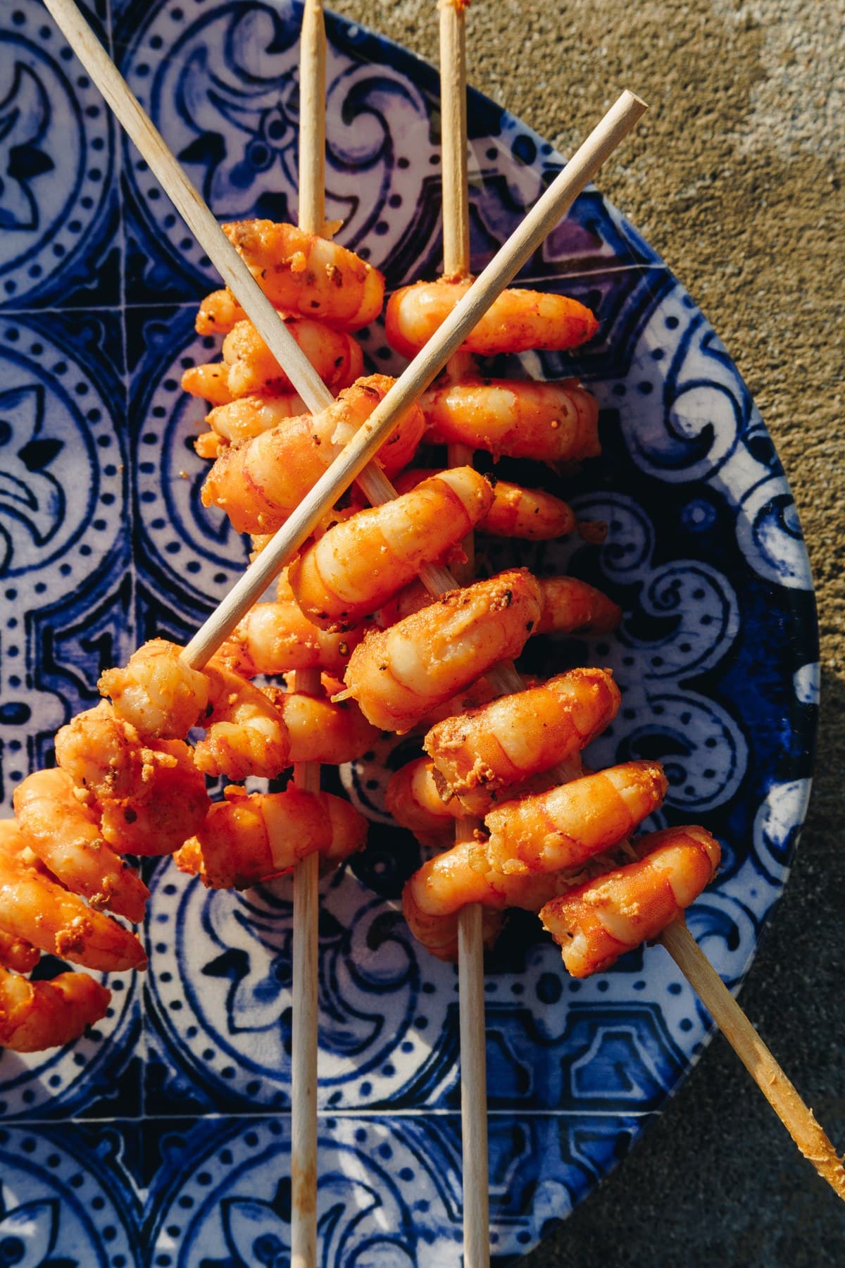 Grilled prawns on wooden skewers over a blue and white patterned plate