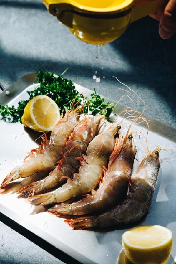Raw whole prawns on a steel tray with lemon halves and parsley