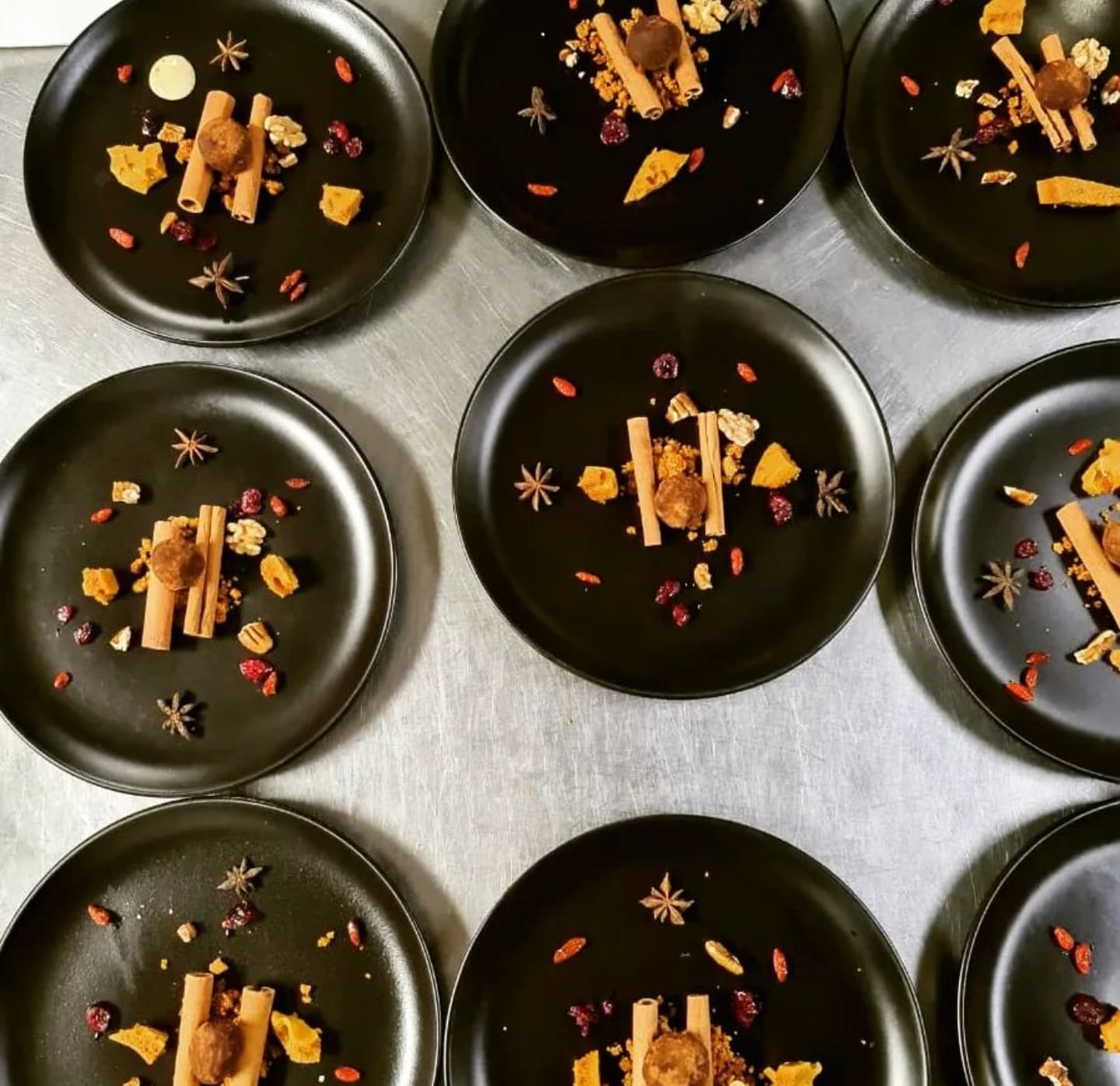 Black dessert plates arranged across a stainless-steel pass