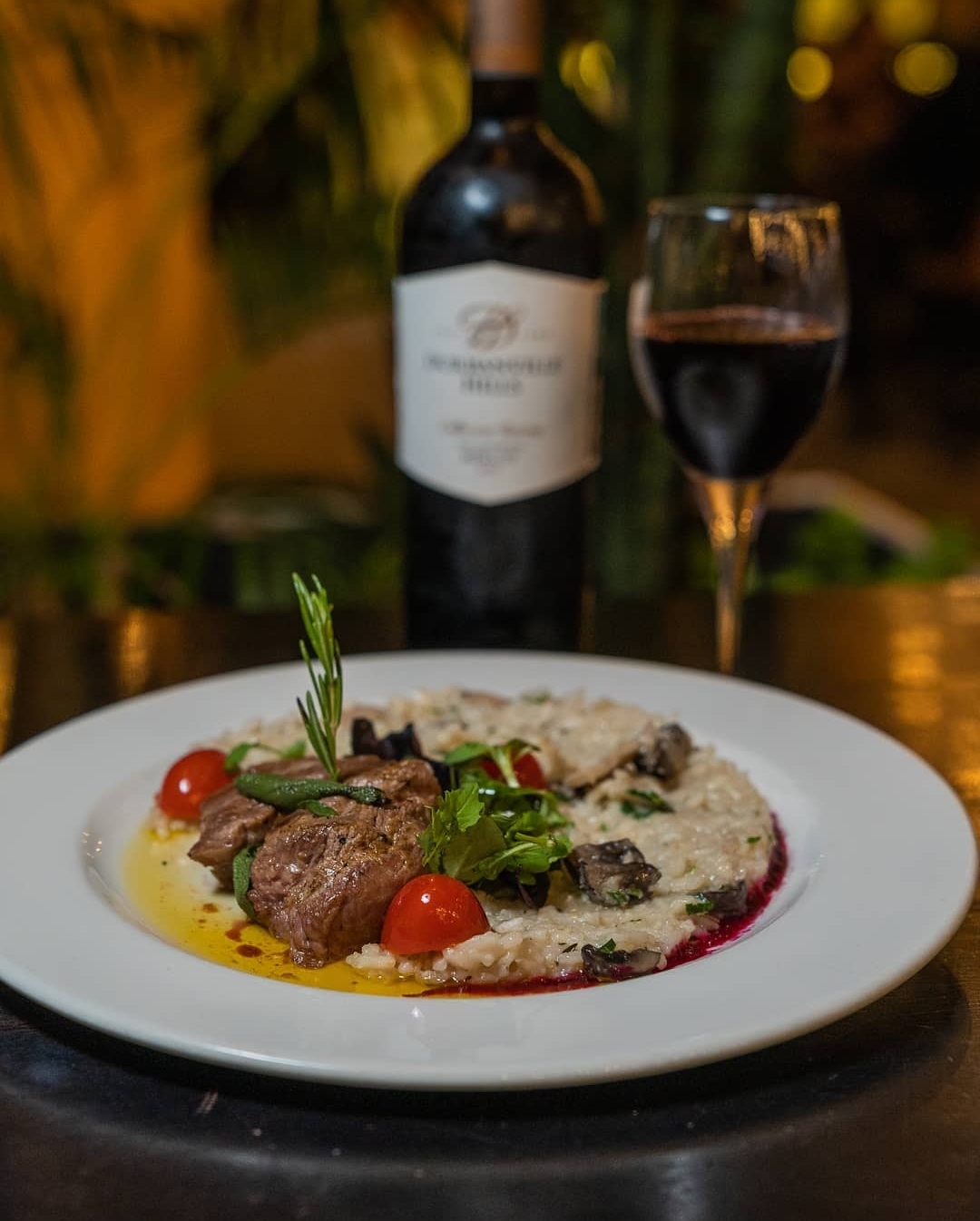 A plated restaurant dish with red wine in warm evening light